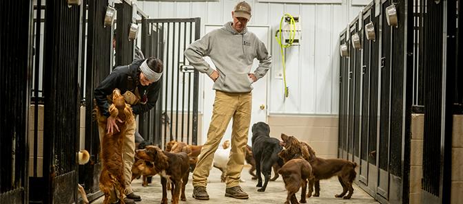 two men petting dogs in front of kennels